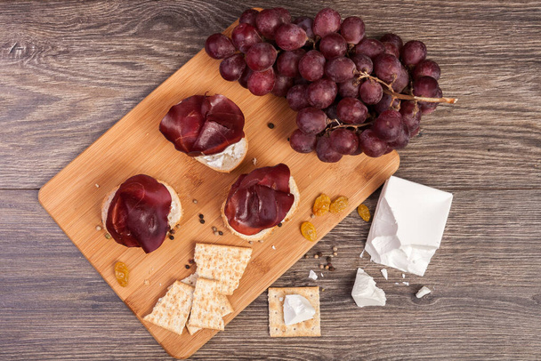 Λευκό τυρί, κροτίδες και το ζαμπόν σε ξύλινο υπόβαθρο. Υγιεινά τρόφιμα - Φωτογραφία, εικόνα