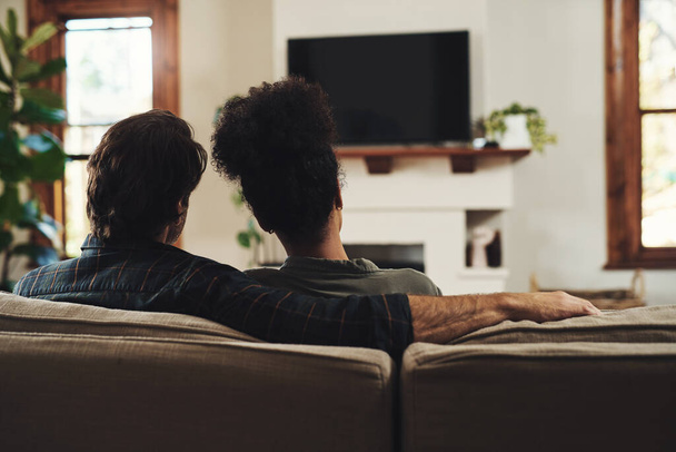 Youre all the company I ever need. Rearview shot of a young couple sitting on sofa and watching tv together at home - 写真・画像