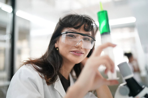 Laboratuvarda mikroskopla çalışan üniformalı genç kadın doktor analiz yapıyor. - Fotoğraf, Görsel