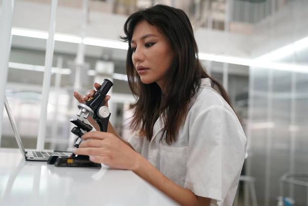 研究室で顕微鏡解析を行う制服を着た若い女性医師 - 写真・画像