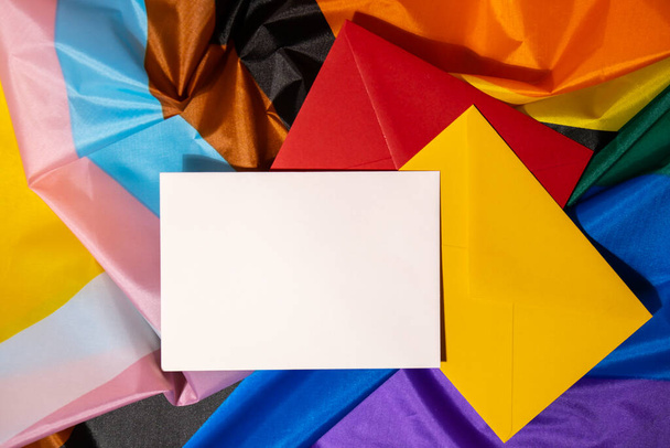 Empty paper blank on Rainbow LGBTQIA flag made from silk material. Mock up template copy space for your text. Symbol of LGBTQ pride month. Equal rights. Peace and freedom. Support LGBTQIA community - 写真・画像