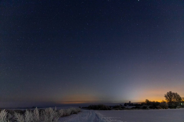 Panorama gwiazd nocą na śniegu, pomarańczowe światła miasta w tle. Wysokiej jakości zdjęcie - Zdjęcie, obraz
