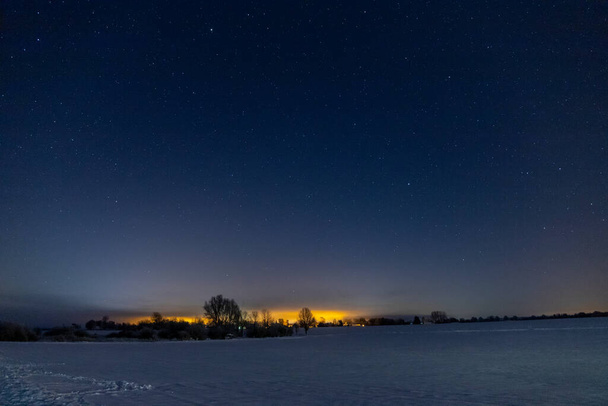 Estrelas panorâmicas à noite na neve, luzes laranja de uma cidade ao fundo. Foto de alta qualidade - Foto, Imagem