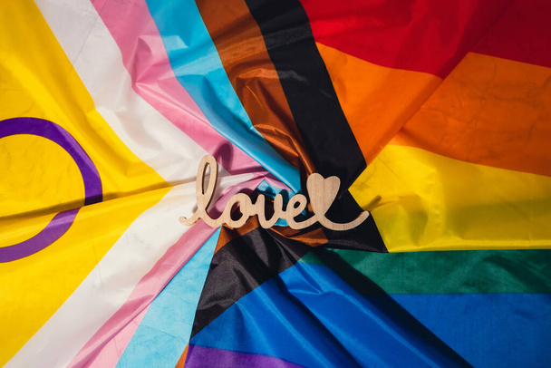 Wooden word love with heart romance on Rainbow LGBTQIA flag made from silk material. Valentines Day greeting card. Symbol of LGBTQ pride month. Equal rights. Peace and freedom. Support LGBTQIA - Photo, Image