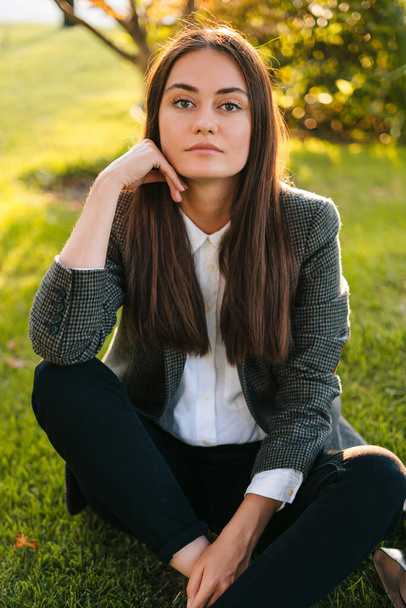 Portret profesjonalnej, pięknej, pewnej siebie, młodej kobiety biznesu siedzącej i patrzącej w kamerę, na pięknym polu zielonej trawy. Styl życia ludzi. Piękność - Zdjęcie, obraz