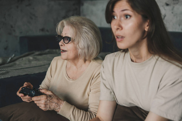 Podekscytowane tysiąclecia dwie kobiety z gamepadami grające w gry wideo we wnętrzu salonu, siedzące na podłodze. Szczęśliwe emocje, wolny czas i rozrywka - Zdjęcie, obraz