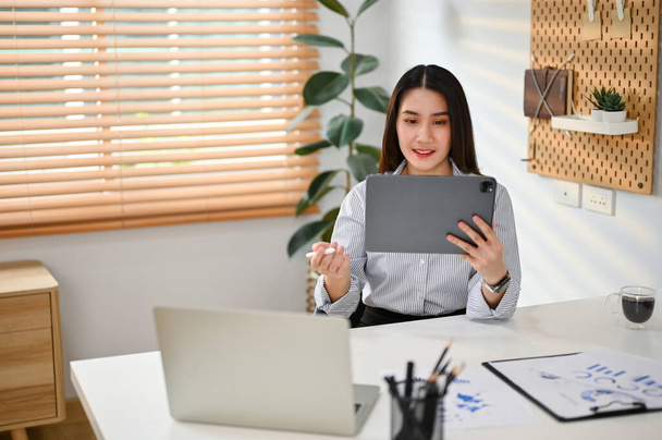 Konzentrierte junge asiatische Büroangestellte, die ihr digitales Tablet am Schreibtisch benutzt und ihr Geschäftsprojekt managt. - Foto, Bild