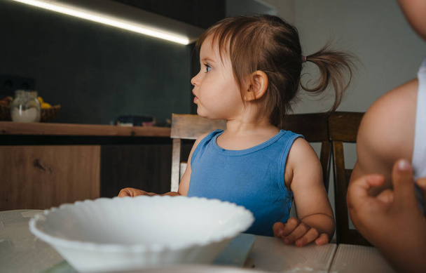 Happy young baby girl baking sweet bicsuits together with her brother in kitchen at home. Cooking, baking, enjoying time with children concept. - 写真・画像