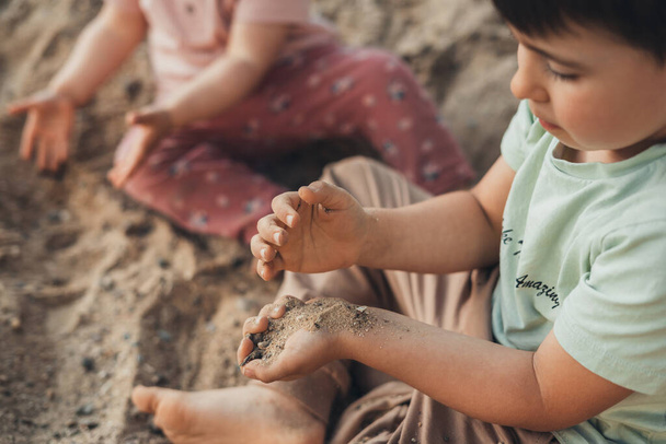 Aranyos fiatal fiú és a kishúga szórakoznak a homokos földön a meleg és napos nyári napon. A gyerek játszik. Nyári tevékenységek gyermekek számára. - Fotó, kép