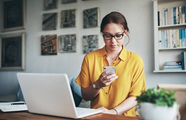 Aktualisierung der Social-Media-Seite für Unternehmen. eine attraktive junge Geschäftsfrau, die allein in ihrem Home Office sitzt und auf ihrem Handy SMS schreibt - Foto, Bild