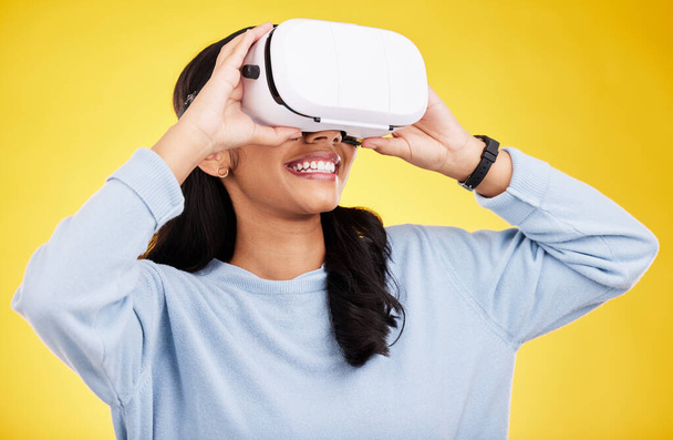 Woman with VR goggles, smile and experience in metaverse, digital world and futuristic on yellow studio background. Virtual reality, technology and UX, happiness and cyber space with gaming. - Фото, изображение