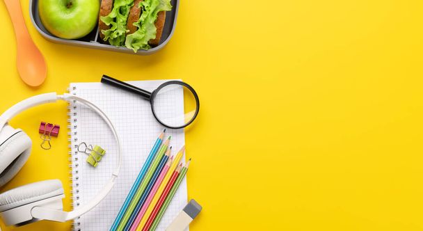 School supplies, stationery, and lunch box on yellow background. Education and nutrition. Flat lay with blank space - Foto, Imagen