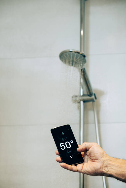 Smart home concept: man controlling warm water temperature using app on his phone - Foto, Imagen