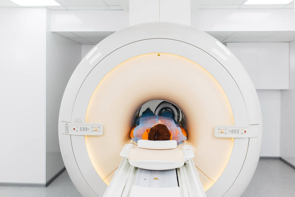 Lékař udělá MRI kolenního kloubu. Mladý pacient na automatickém stole vychází z uzavřeného přístroje na magnetickou rezonanci. Moderní vybavení, cívka na koleni pacienta. - Fotografie, Obrázek