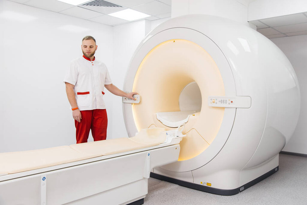 Ένας γιατρός κάνει μαγνητική τομογραφία ή τομογραφία PET ενός ασθενούς σε μια σύγχρονη κλινική. Μαγνητική τομογραφία στη μελέτη του ανθρώπινου σώματος. Ο γιατρός ετοιμάζει τη συσκευή για αξονική τομογραφία - Φωτογραφία, εικόνα