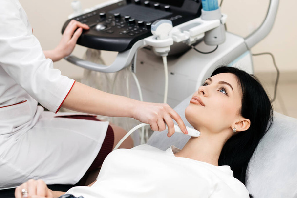 Ultrasound diagnosis of the thyroid gland of a young woman in the clinic. A female doctor holds an ultrasound probe along the patient's neck. Health concept. - Foto, afbeelding