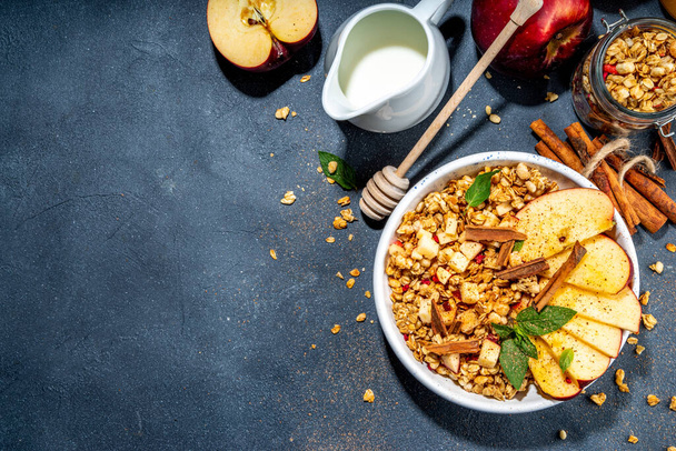 Healthy autumn breakfast granola. Apple pie granola with muesli, cinnamon spices, apples slices, honey and nuts, on black stone background copy space - 写真・画像