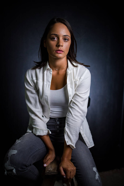 Pretty dark haired girl posing for a fashion shoot in a studio. She is dressed in stylish jeans and a crop top, and her poses convey a sense of youthfulness and vitality. - Fotografie, Obrázek