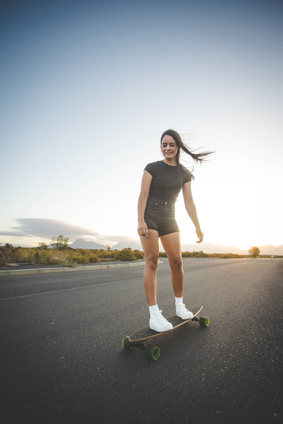 pretty young woman with dark hair skateboarding in a vibrant urban environment. - Фото, зображення