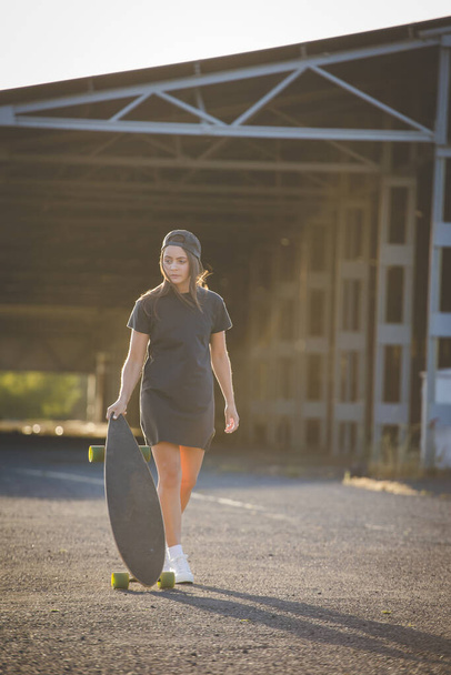 mooie jonge vrouw met donker haar skateboarden in een levendige stedelijke omgeving. - Foto, afbeelding