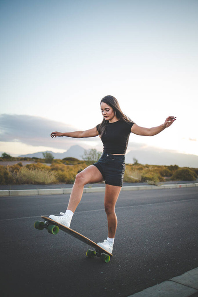 pretty young woman with dark hair skateboarding in a vibrant urban environment. - Photo, Image