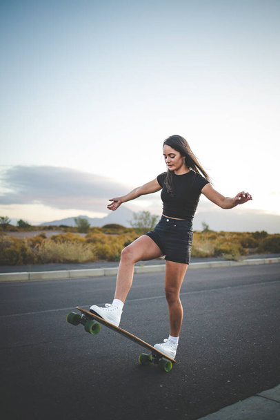 pretty young woman with dark hair skateboarding in a vibrant urban environment. - Foto, immagini