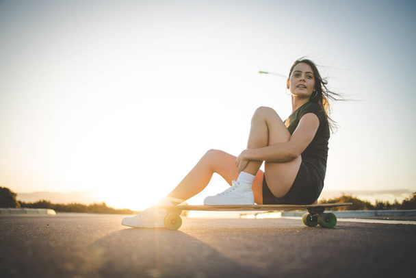pretty young woman with dark hair skateboarding in a vibrant urban environment. - Φωτογραφία, εικόνα
