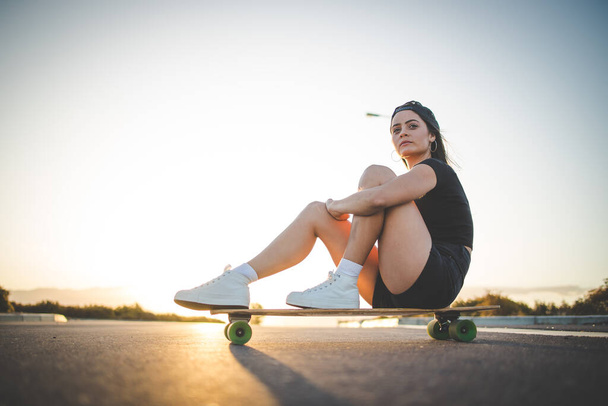 pretty young woman with dark hair skateboarding in a vibrant urban environment. - Foto, afbeelding
