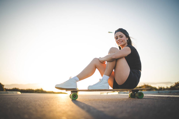 pretty young woman with dark hair skateboarding in a vibrant urban environment. - Фото, изображение
