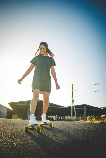 pretty young woman with dark hair skateboarding in a vibrant urban environment. - Foto, Imagen
