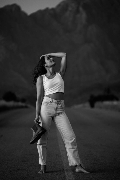 pretty young woman with dark hair on a deserted road. She is dressed in trendy and fashionable attire, including jeans and a stylish crop top. - Foto, immagini