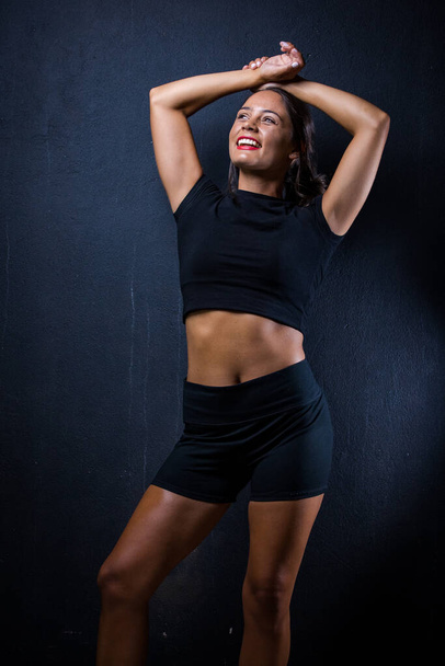 pretty dark haired girl posing for a fitness photo shoot in a studio. She is dressed in tight shorts and a crop top, and her poses convey a sense of strength, athleticism, and fitness.  - Фото, изображение