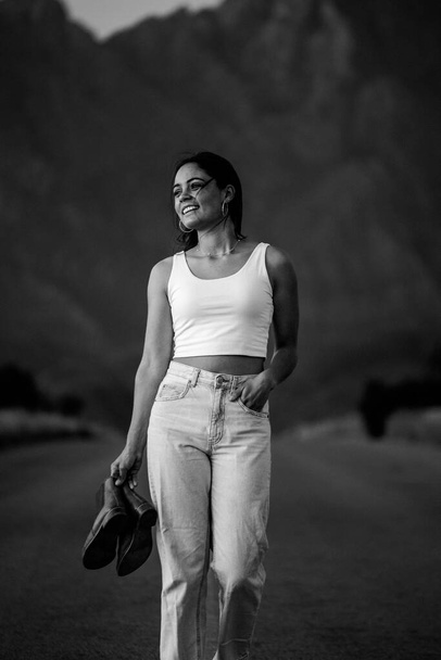 pretty young woman with dark hair on a deserted road. She is dressed in trendy and fashionable attire, including jeans and a stylish crop top. - Foto, imagen
