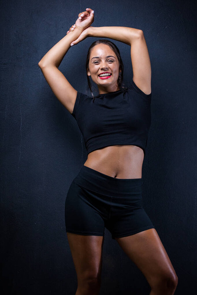 pretty dark haired girl posing for a fitness photo shoot in a studio. She is dressed in tight shorts and a crop top, and her poses convey a sense of strength, athleticism, and fitness.  - Fotografie, Obrázek