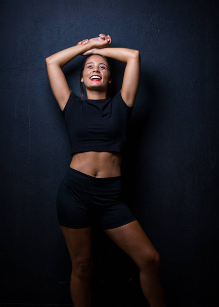 pretty dark haired girl posing for a fitness photo shoot in a studio. She is dressed in tight shorts and a crop top, and her poses convey a sense of strength, athleticism, and fitness.  - Foto, Imagen