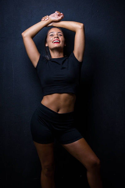 pretty dark haired girl posing for a fitness photo shoot in a studio. She is dressed in tight shorts and a crop top, and her poses convey a sense of strength, athleticism, and fitness.  - Fotó, kép
