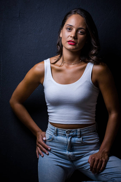 Pretty dark haired girl posing for a fashion shoot in a studio. She is dressed in stylish jeans and a crop top, and her poses convey a sense of youthfulness and vitality. - Fotó, kép