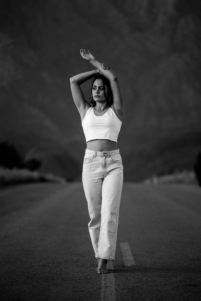 pretty young woman with dark hair on a deserted road. She is dressed in trendy and fashionable attire, including jeans and a stylish crop top. - 写真・画像