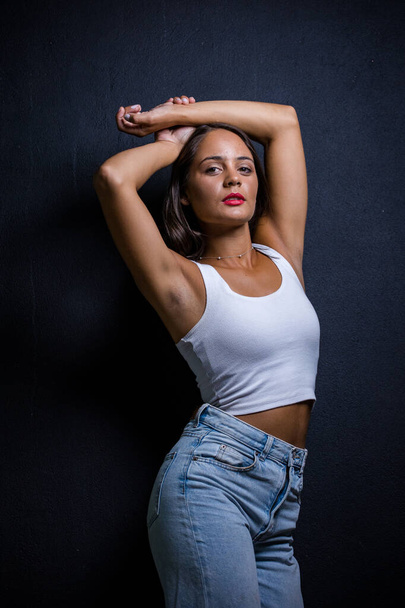 Pretty dark haired girl posing for a fashion shoot in a studio. She is dressed in stylish jeans and a crop top, and her poses convey a sense of youthfulness and vitality. - Valokuva, kuva