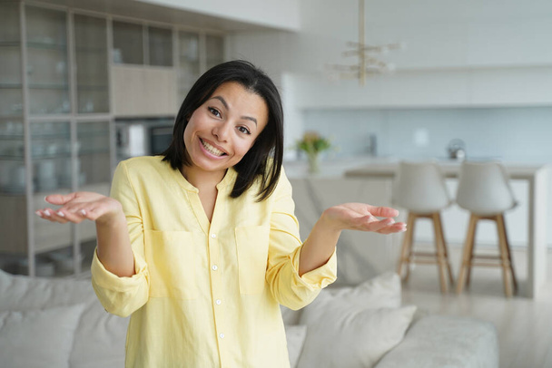 Cute happy puzzled woman, dont know concept. Portrait of young european woman showing positive emotions. Advertising banner mockup. Confused girl in living room at home. Modern interior of apartment. - Foto, Imagen