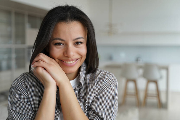 Smiling young female homeowner or apartment renter pose looking at camera at home. Happy shy brunette woman feels tender emotion, folded hands near cheek in new house. Mortgage, real estate sale. - Fotoğraf, Görsel