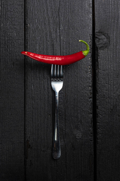 A red chili pepper on a fork on a black table. - Fotoğraf, Görsel