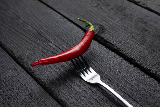 A red chili pepper on a fork on a black table. - Foto, Imagem