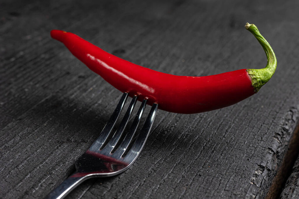 A red chili pepper on a fork on a black table. - Foto, afbeelding