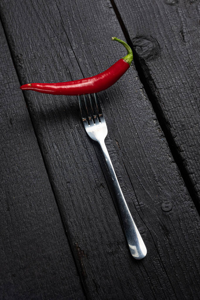 A red chili pepper on a fork on a black table. - Φωτογραφία, εικόνα