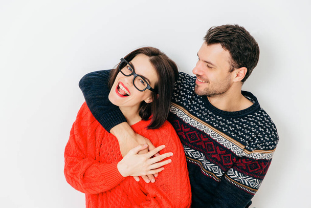 Romantic couple in love embrace each other and have fun together, wear warm knitted sweaters, stand against white background. Cheerful woman and man enjoy togetherness. Relationship concept. - Foto, Imagem