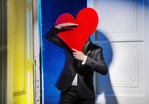 Cheerful man hiding himself behind a heart - Fotoğraf, Görsel