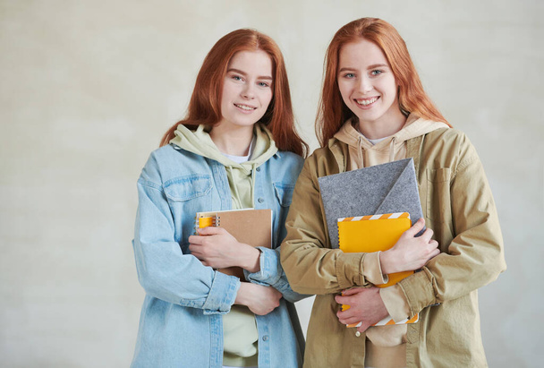 Horizontal medium studio portrait of two modern twin college students wearing casual clothes holding textbooks smiling at camera - Zdjęcie, obraz