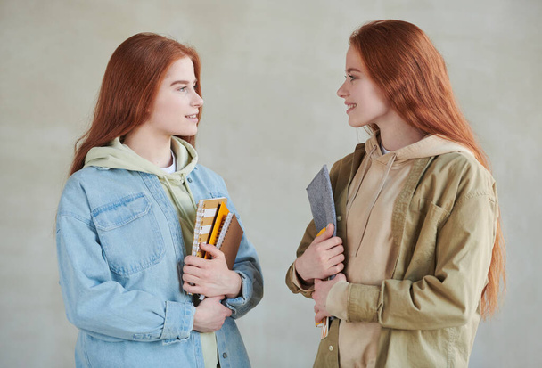 Vaaka keskipitkän studio muotokuva kaksi modernia twin naispuolinen yliopisto-opiskelijoille yllään rento vaatteita tilalla oppikirjoja katsellen toisiaan - Valokuva, kuva