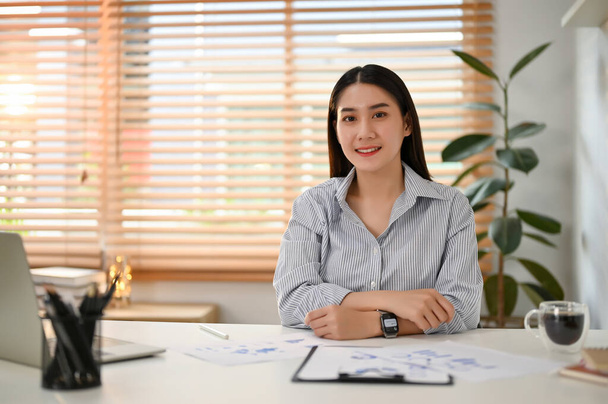 Attraente e sorridente giovane asiatica imprenditrice o impiegata si siede alla scrivania del suo ufficio nel suo ufficio privato. - Foto, immagini